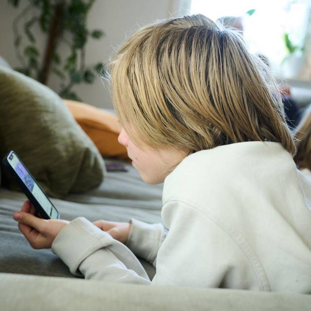 Junge liegt auf einem Sofa und guckt auf sein Smartphone