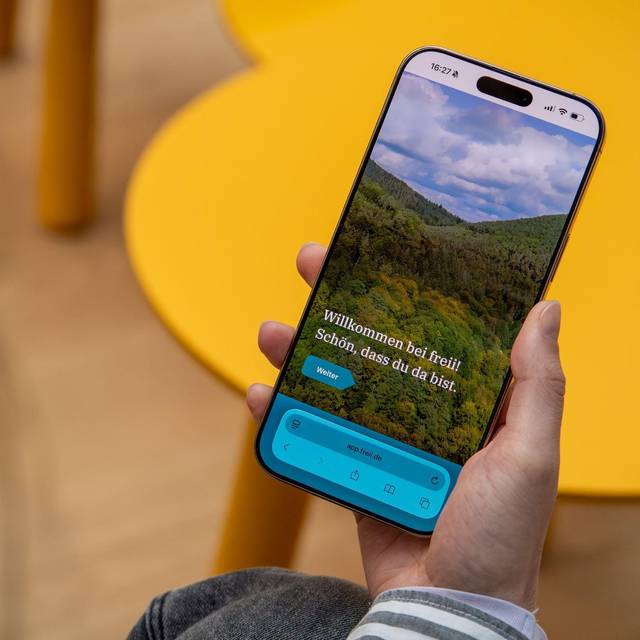 Eine Frau haelt ein Handy mit der Web-App «freii» in der Hand
