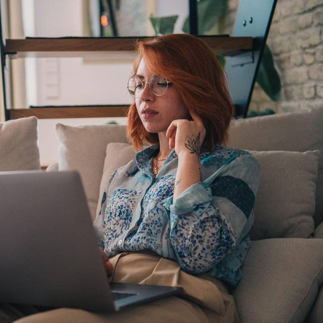 Eine Frau sitzt auf der Couch und nutzt einen Laptop