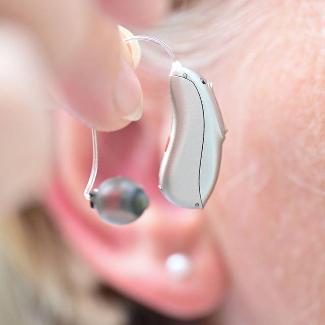 Eine Frau hält ein Hörgerät vor ihr Ohr