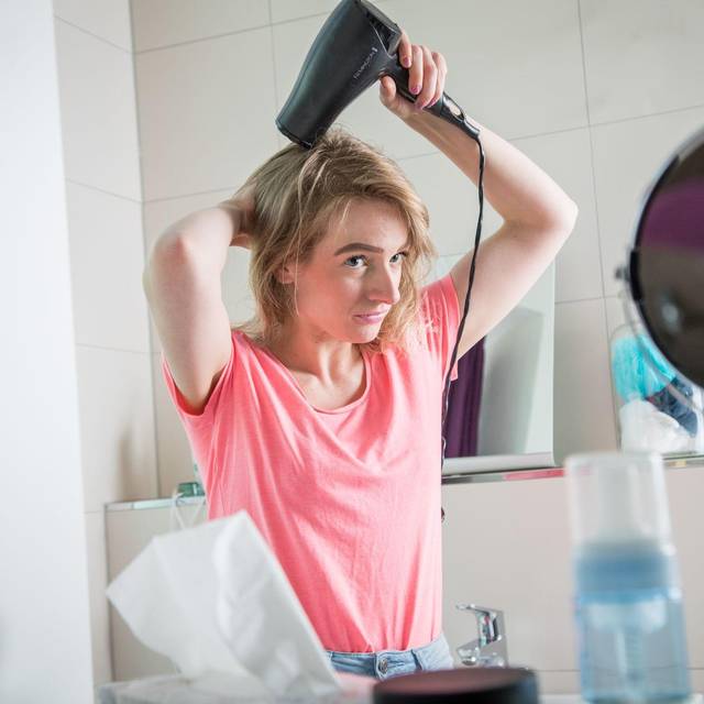 Eine junge Frau föhnt ihre Haare