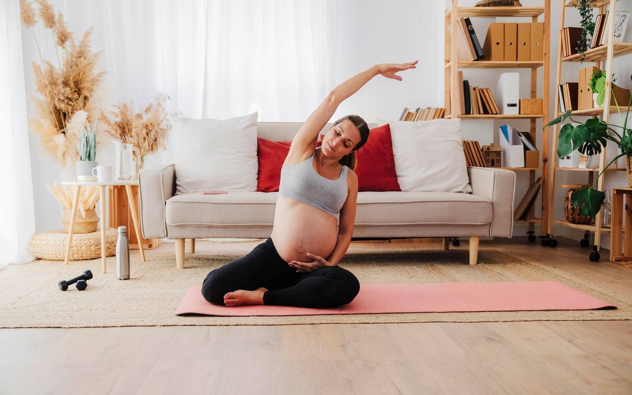 Eine Schwangere macht Dehnübungen auf einer Yogamatte