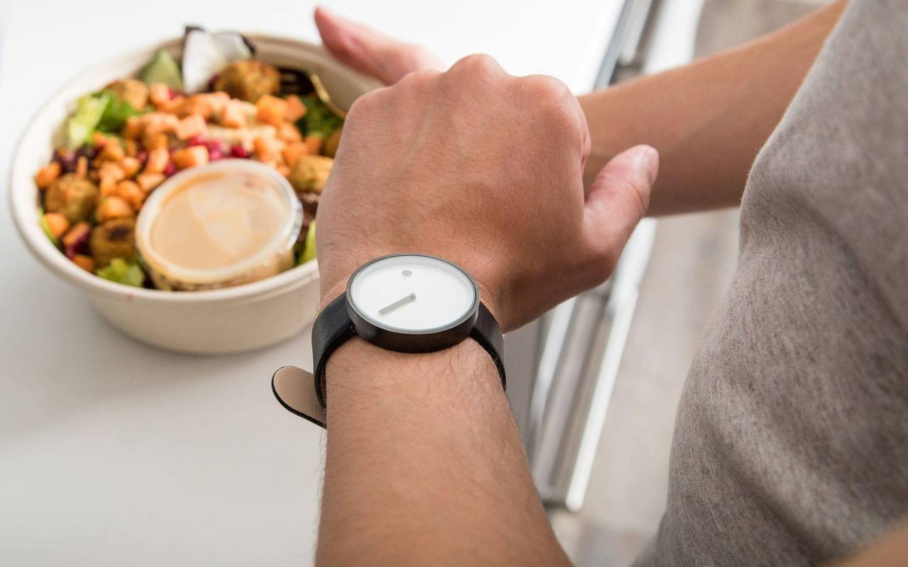 Ein Mann mit einem Teller in der Hand sieht auf seine Uhr
