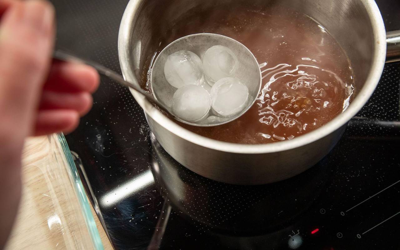 Eiswürfel in einer Suppenkelle werden über Brühe gehalten