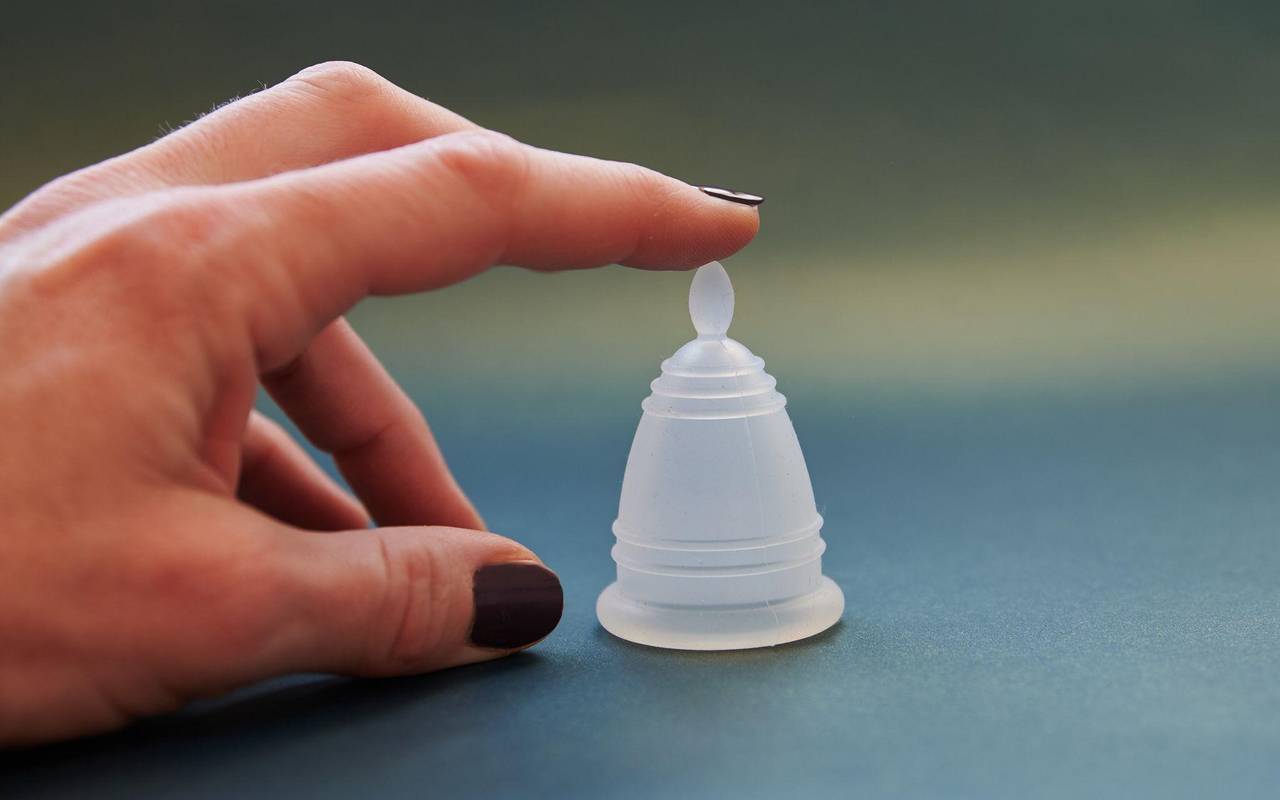 Eine Frau zeigt auf eine Menstruationstasse