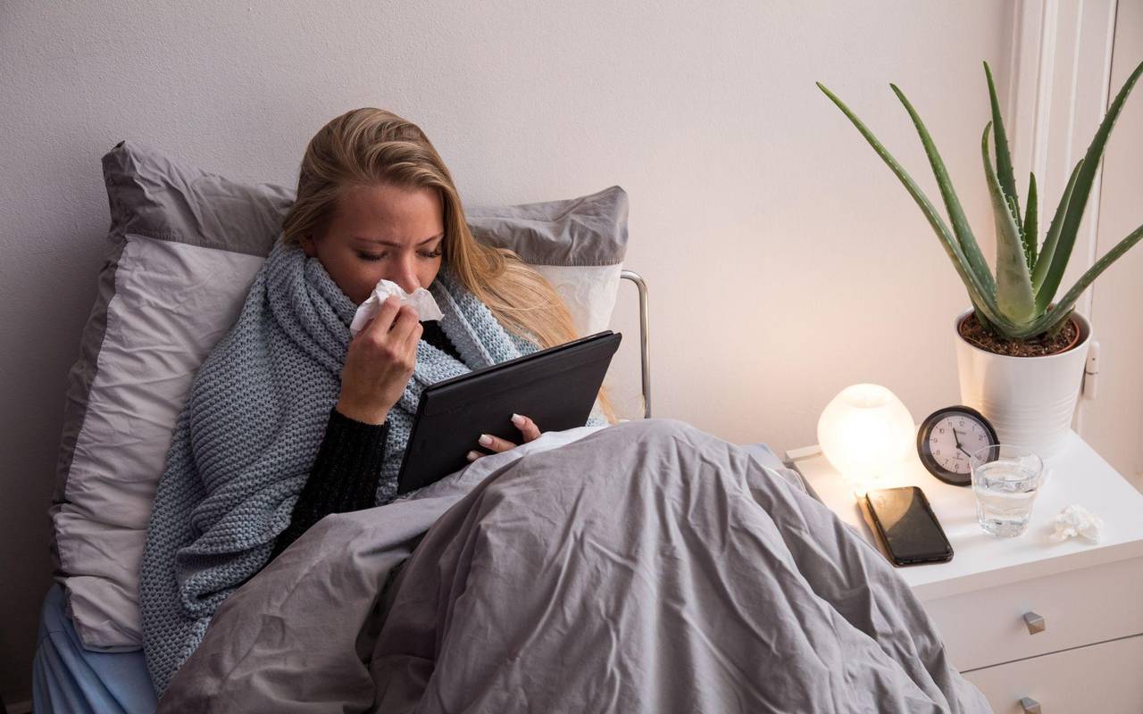Eine Frau liegt krank im Bett und guckt auf ihren Tablet-Computer