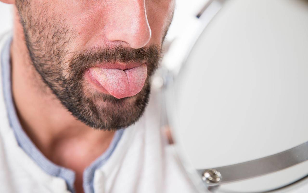 Mann betrachtet seine Zunge im Spiegel