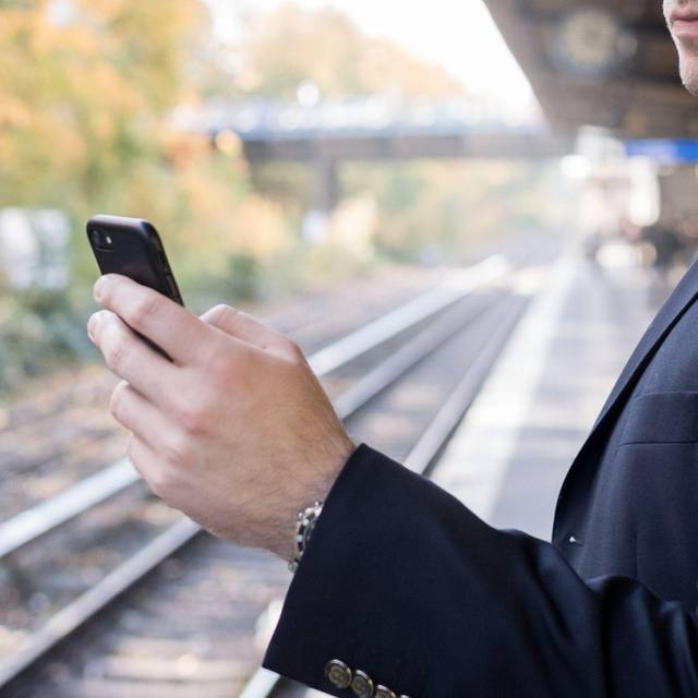 Mann mit Smartphone am Gleis