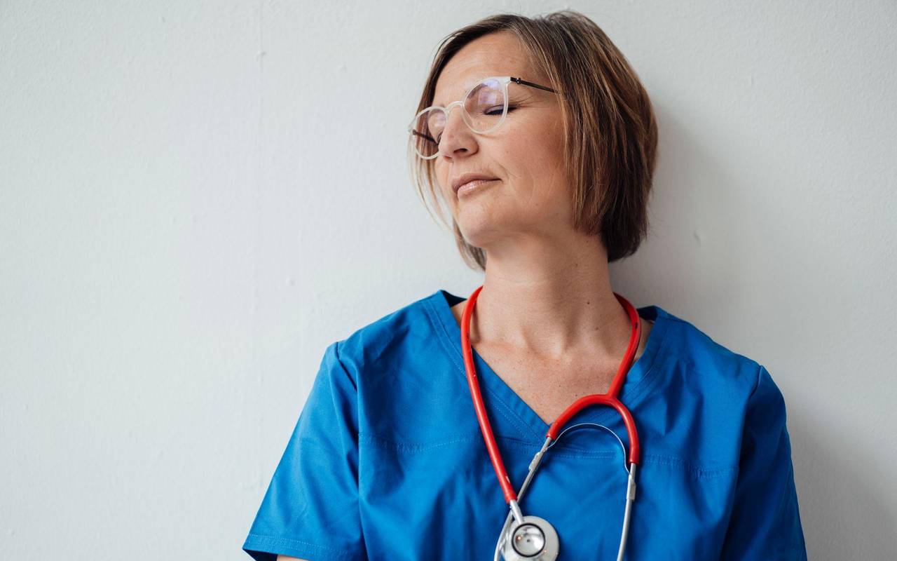 Eine Ärztin lehnt mit geschlossenen Augen an der Wand
