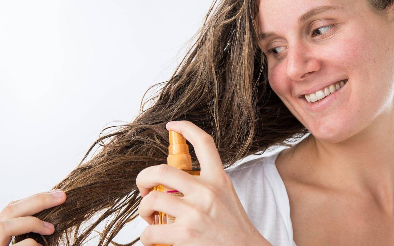 Eine Frau sprüht sich mit einem Haarpflegeprodukt auf die Haare