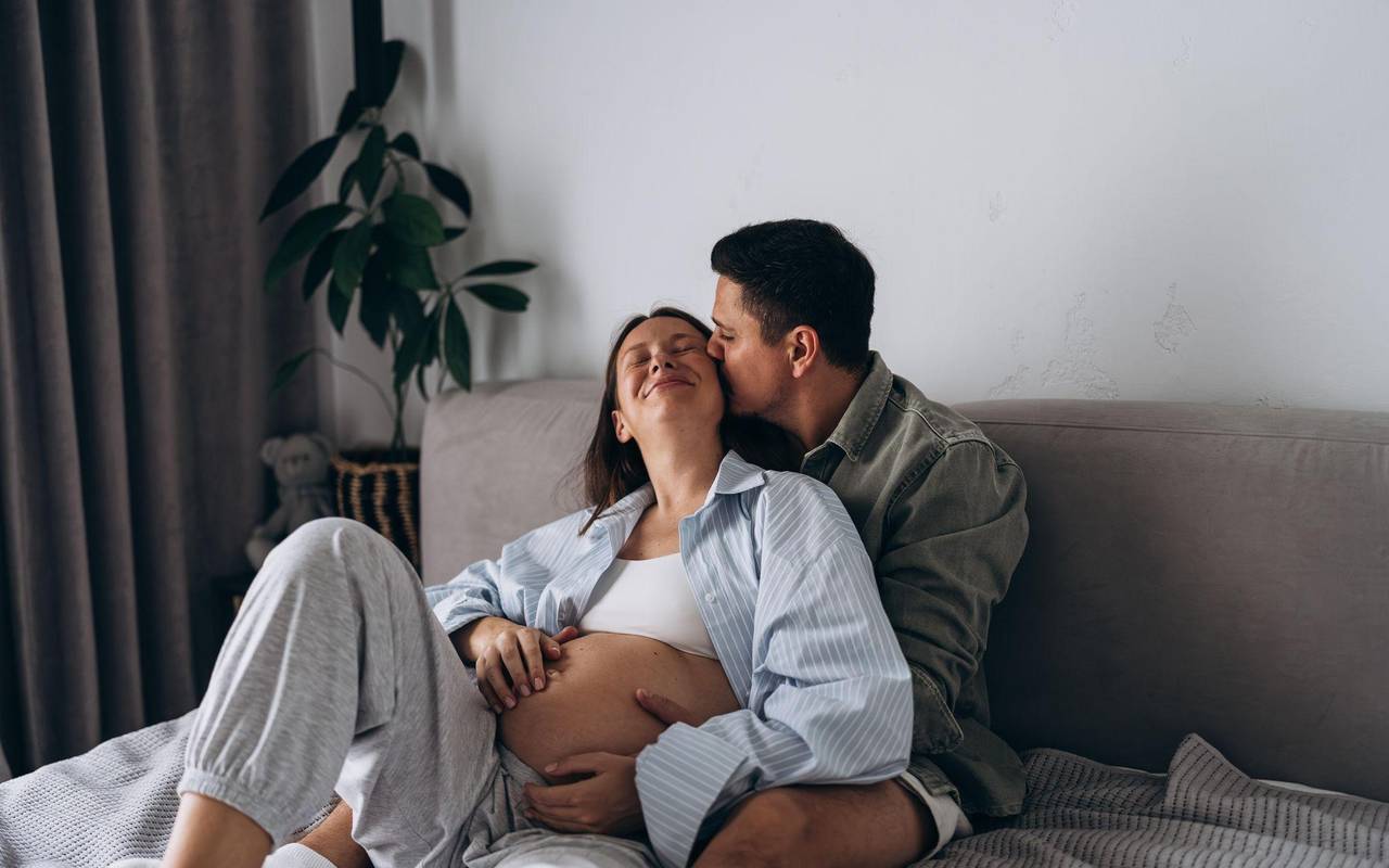 Eine schwangere Frau liegt mit ihrem Partner kuschelnd im Bett