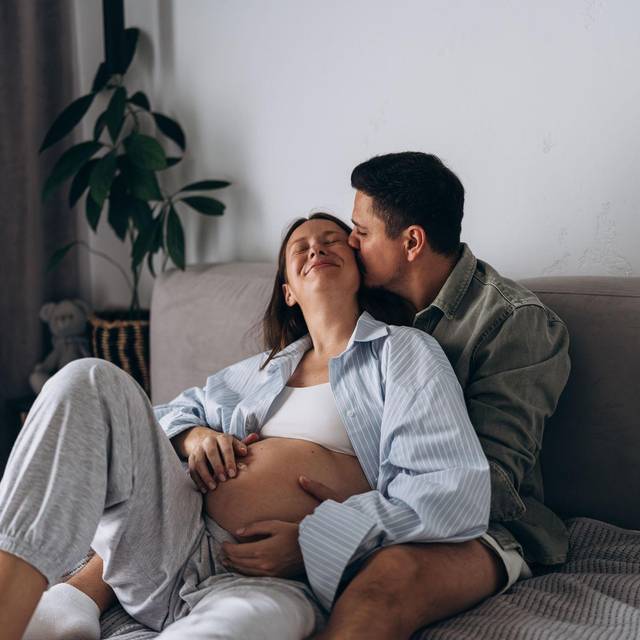Eine schwangere Frau liegt mit ihrem Partner kuschelnd im Bett