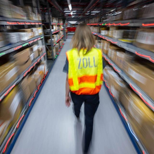 Eine Zollbeamtin läuft durch ein Paketlager