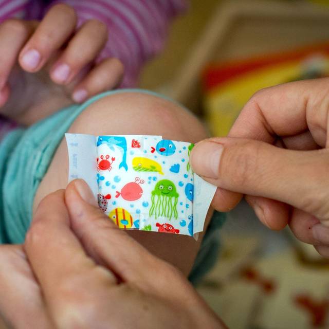 Eine Mutter klebt ihrer Tochter ein buntes Pflaster aufs Knie