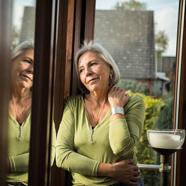 Eine ältere Frau schaut gedankenverloren aus dem Fenster