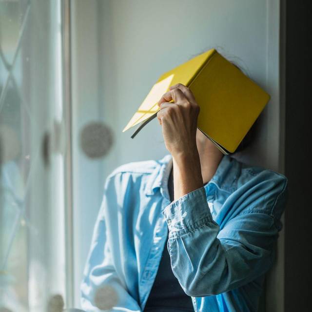 Eine Frau verbirgt ihr Gesicht hinter einem Notizheft