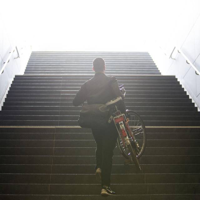Mann trägt sein Fahrrad eine Treppe hinauf