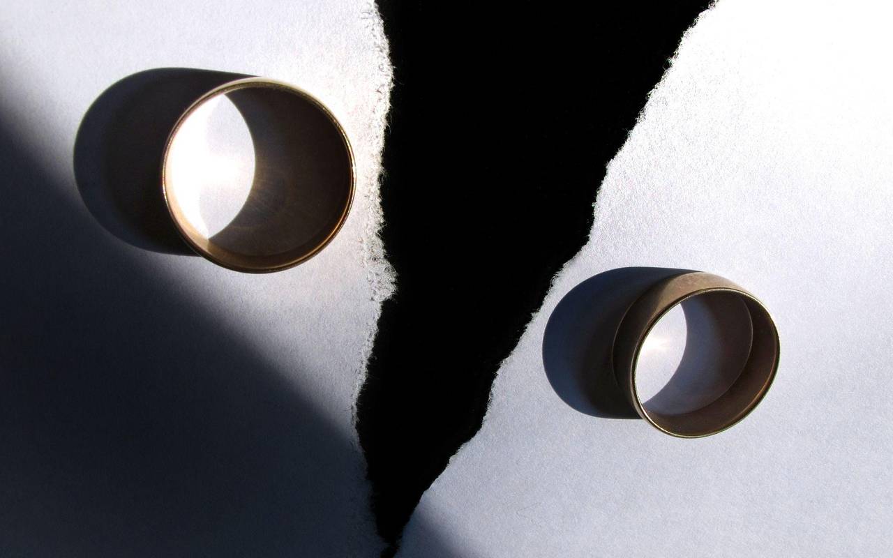 Zwei getragene Eheringe liegen auf einem zerrissenen Papier