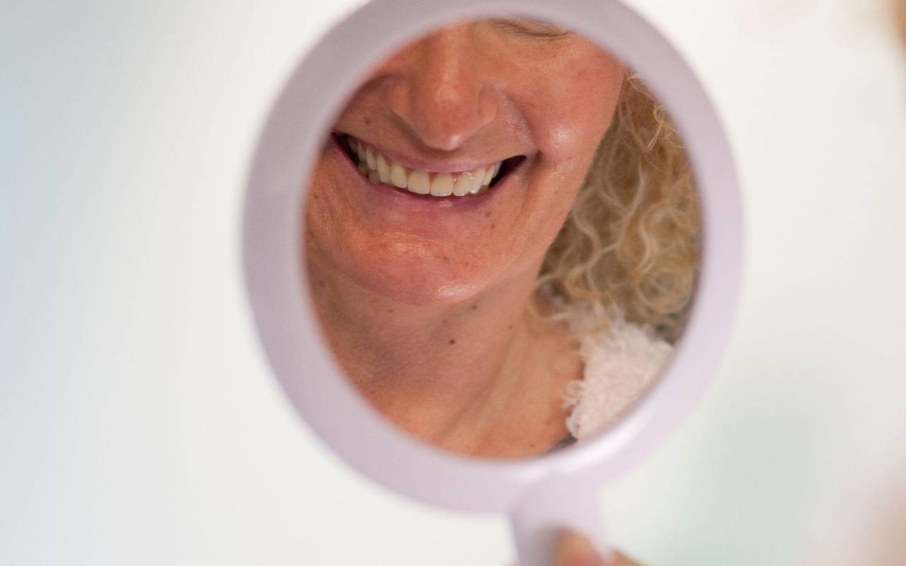 Frau schaut sich ihre Zähne in einem Handspiegel an