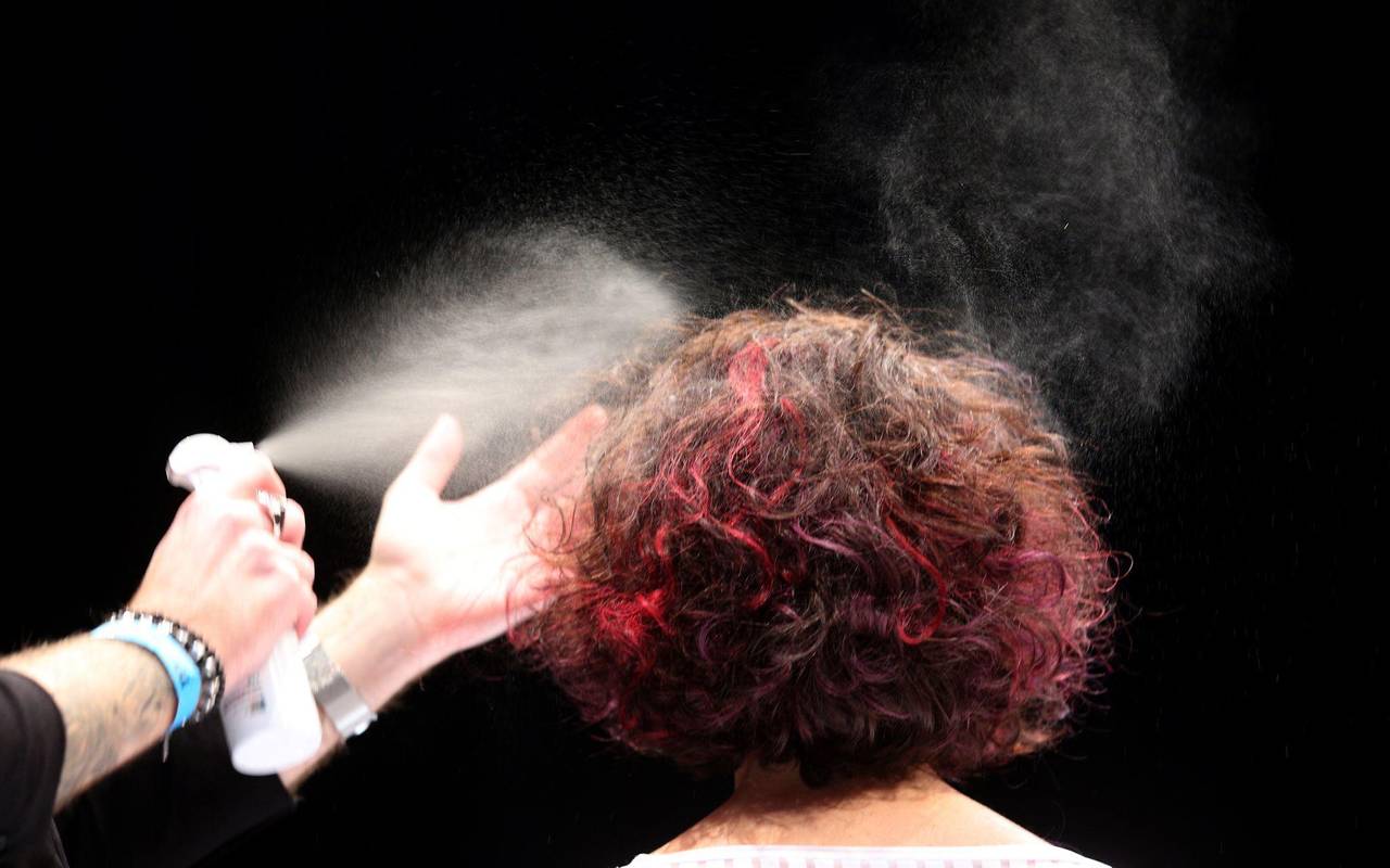 Ein Friseur sprüht einer Frau die Haare mit Haarspray ein