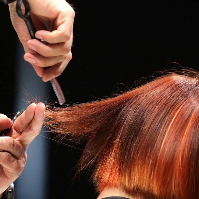 Ein Friseur schneidet einer Frau mit roten Haaren die Haare