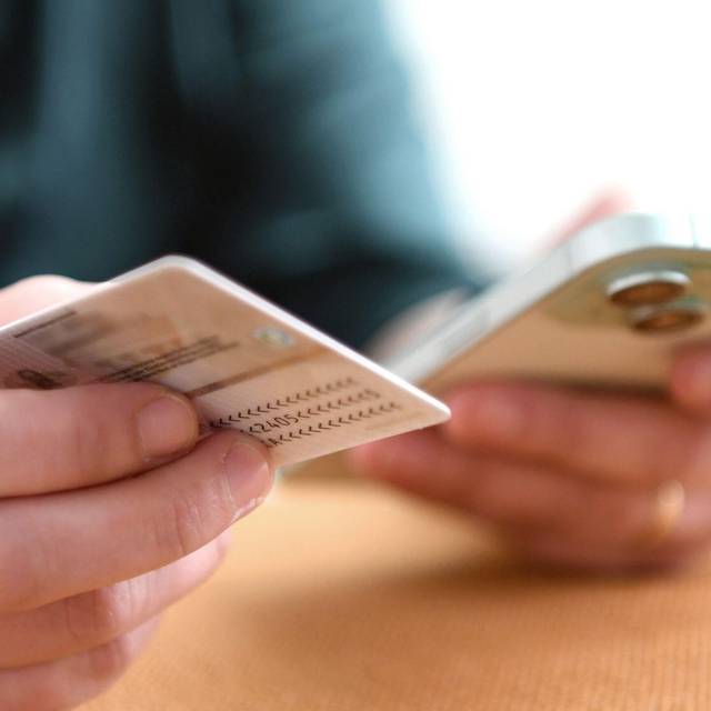Eine Frau hält Personalausweis und Smartphone in den Händen